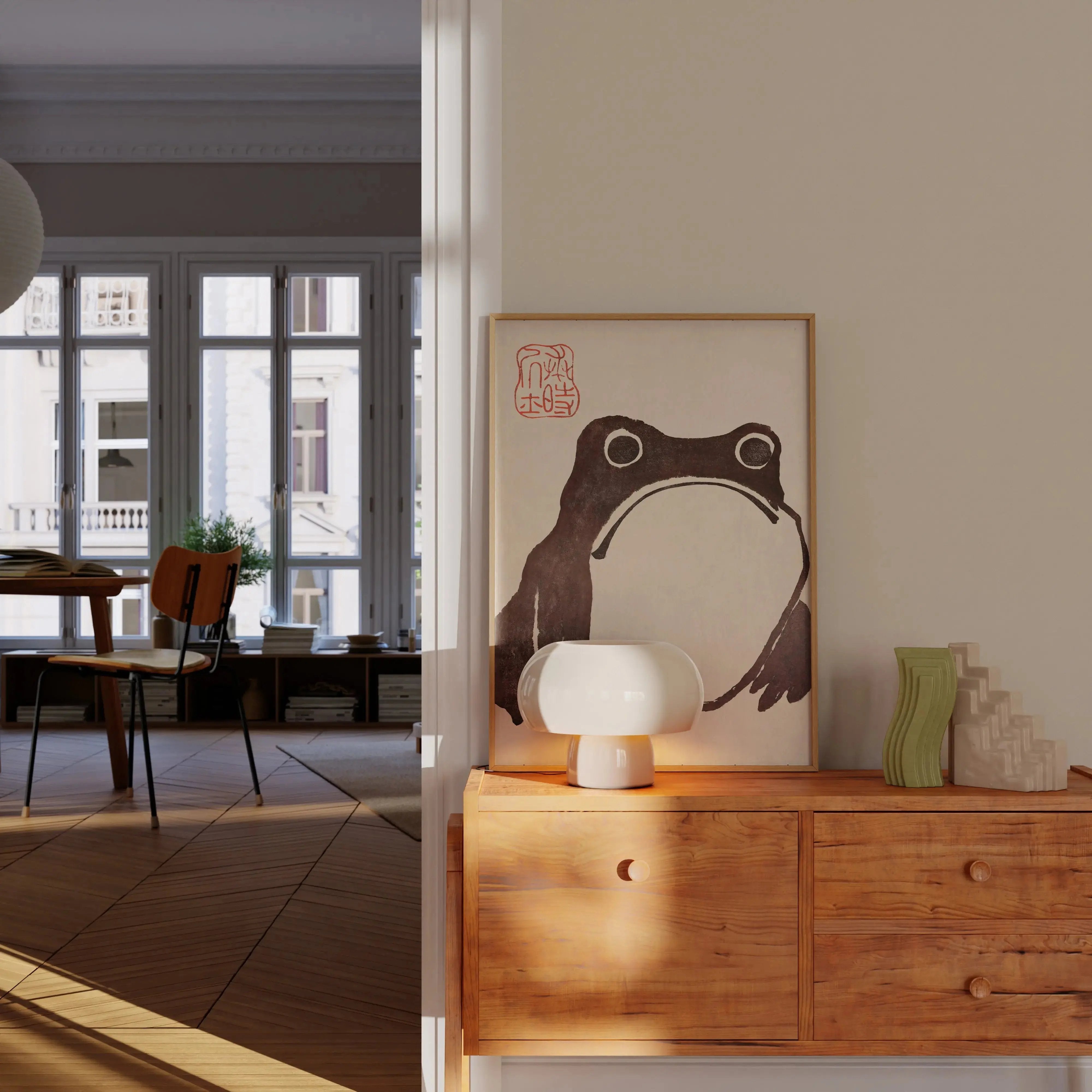 Japanese wall art print “The Frog,” a minimalist black-and-white frog illustration in a light wood frame displayed on a wooden console next to a white lamp